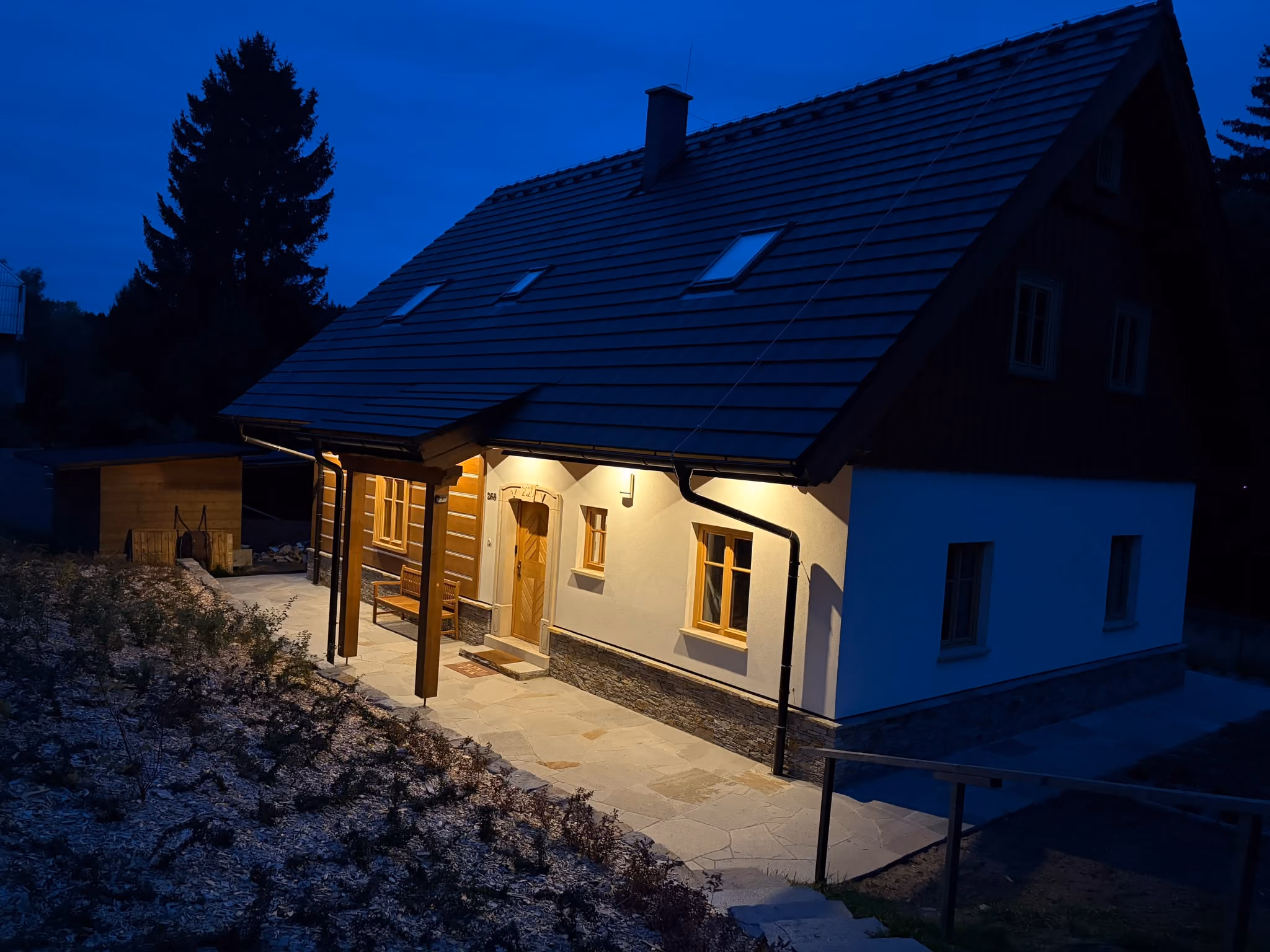 Omítnutá strana se vstupem a kamennou dlažbou večer